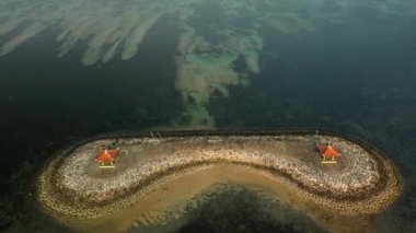 Bali 'deki Sanur sahilinin açıklarında yapay olarak yaratılmış bir adanın havadan görüntüsü. Küçük insan yapımı bir adada, sakin turkuaz okyanus suyuyla çevrili iki çardak var. Bali 'nin en iyi plajları.