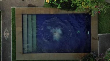 Havuza atlayan ve su sıçrayan genç bir kadının tepeden aşağı görüntüsü. İyi tatiller ve hayatın tadını çıkarma kavramı. Havuzda oynaşan neşeli kadın, mutlu zaman..