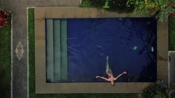 在空中看到一个穿着红色比基尼的年轻漂亮的女人在游泳池里放松 享受着她的假期 女人抬起头来笑了 热带国家度假的概念与自由 — 图库视频影像