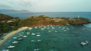 Bali adasındaki Padang Bai limanının okyanus manzaralı sahili. Yeşil tepelerin arka planına ve limana yakın beyaz bir plaja karşı gün batımı. Balıkçı tekneleri suya park edilmiş..