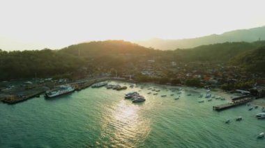 Bali adasındaki Padang Bai limanında, iskeleye demirlemiş büyük bir feribottan ateş ediliyor. Arkasında dağlar olan pitoresk bir liman. Bir sürü küçük balıkçı teknesi..