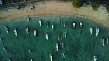 Limanın kuş bakışı manzarası ve okyanus kenarına park edilmiş renkli balıkçı tekneleri. Bali adasındaki Padang Bai limanına yakın bir sahil. Sahilde gün batımında sayısız tekne.