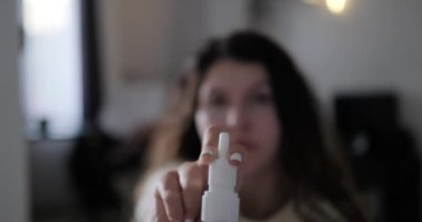 Ön planda, arka planda kadın yüzü olan akıcı bir burnu tedavi etmek için burun spreyi sıkmak var. Sprey ışığı yavaş çekimde düşürür. Burun akıntısı ve sinüzit tedavisi.