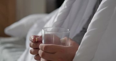 Sakallı hasta bir adam, beyaz bir battaniyeye sarılmış, bir hap alıyor ve onu suyla yıkıyor. Şiddetli soğuk algınlığı ve grip tedavisi. Hastalıkların ve antibiyotiklerin tedavisi.