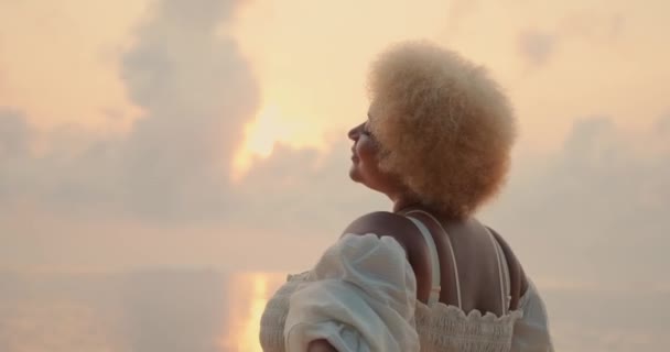 一位年轻的非洲裔美国女人 一头卷曲的金发 身穿白色连衣裙 享受海边的日出 张开双臂旋转着 美好的一天开始了 — 图库视频影像