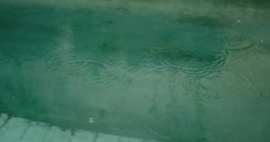 Havuz suyunun yüzeyine düşen yağmur damlalarının yakın çekim görüntüsü bir sıçrama yaratıyor. Yağmurlu, doğal bir arka plan. Meditasyon ve huzur.