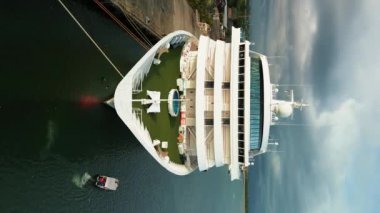 Hava görüntüsü, tropik bir adada limandan kalkmayı bekleyen büyük bir yolcu gemisinin dikey videosu. Bir yolcu gemisinde tatil ve Güneydoğu Asya adalarına seyahat..