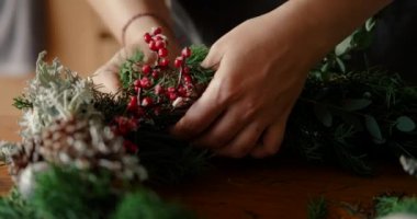 Kırmızı böğürtlenli dalla Advent çelengi süsleyen genç bir kadının yakın çekimi. Yeni yıl ve Noel için el yapımı dekorasyonlar, özel ders..