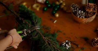 Elinde tel makası olan genç bir kadın Noel çelengi yapmak için ladin ağacından dallar kesiyor. Noel ve Yeni Yıl için dekorasyon üzerine atölye.