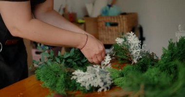 Genç bir kadının elleri ladin ve çam dallarından bir kompozisyon oluşturur ve onlardan bir Noel çelengi yapar. Noel süslemeleri oluşturma ve tatil için hazırlanma süreci.