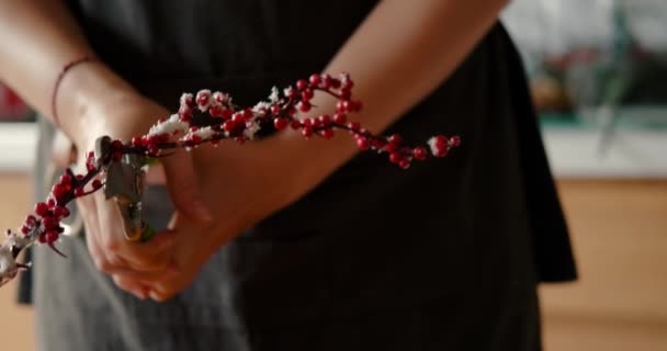 赤い装飾的な果実を持つ枝は クリスマスのための花輪を作るために枝の一部を切り取るためにプライヤーを使用する若い女性の手にあります 休日のための家を準備し — ストック動画