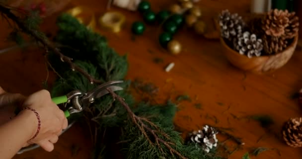 一位手里拿着钢丝钳的年轻女子从云杉树上砍下树枝 做成圣诞花圈 圣诞及新年装饰品制作工作坊 — 图库视频影像