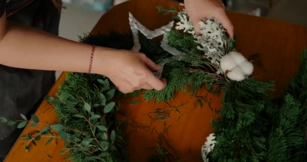 테이블에 전나무 가지에서 크리스마스 화환을 소나무 공으로 여자의 클로즈업 — 비디오