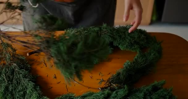 一个年轻女人的小手 她从木桌上的枞树枝上摘下一个圣诞花环 为新年和圣诞节准备装饰品 — 图库视频影像