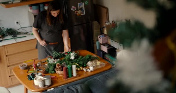 キッチンで自宅にいる若い女性のトップビューは クリスマスのお祝いのために準備し 木製のテーブルの上の枝から羽を作ります 新年のための準備の家庭的な雰囲気 — ストック動画
