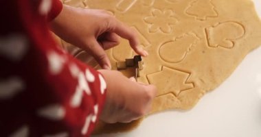 Beyaz bir masanın üzerine yuvarlanmış hamurun yakın plan görüntüsü. Küf kullanan bir kadın zencefilli kurabiye yapıyor. Kardan adam, kar tanesi ve zencefilli kurabiye şeklinde Noel kurabiyeleri..