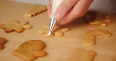 Genç bir kadının elleri, kar tanesi şeklindeki zencefilli kurabiyeyi beyaz kremayla süslerken. Noel kurabiyeleri ve tatil hazırlıkları. Şekerlemeci.