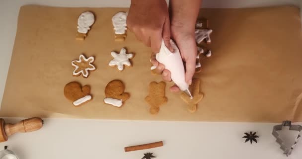 白いアイシングでジンジャーブレッドクッキーを飾った若い女性のトップビュー 雪だるま クリスマスツリーの形をしたクリスマスクッキー 休日のためのデザートの準備 — ストック動画