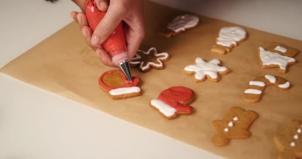 一个年轻女人的手的特写 她用红色的糖霜把姜饼做成手套状 圣诞节甜饼干 形状像雪花和姜饼人 — 图库视频影像