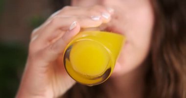 Şeffaf bir bardaktan portakal suyu içen genç bir kadının yakın çekimi. Sıcak yaz sıcağında ferahlatıcı bir içecek. Kahvaltıda vitamin içeceği. Düzgün beslenme kavramı.