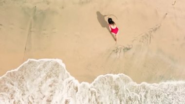 Okyanus kıyısındaki kumlara büyük bir kalp çizen kırmızı mayo giymiş genç bir kadının hava görüntüsü. Sevgililer Günü 'nde ilan-ı aşk. Kuma bir kalp çiz. Balayı.