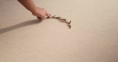 Genç bir kadın okyanus kıyısındaki kuma bir kalp sembolü çiziyor. Sevgililer Günü için ilan-ı aşk. Kuma çizen bir parmağın yakın çekimi. Arka plan videosu, tatil ve tatil konsepti.