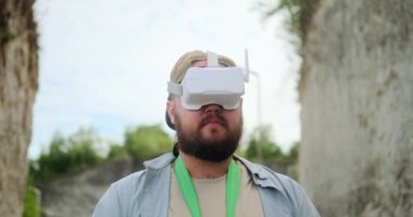 Bir erkek FPV pilotunun portresi kanyonda duruyor ve gözlük kullanarak insansız hava aracını kontrol ediyor. Seyahat ederken ve güzel yerlere uçarken insansız hava aracı fotoğrafçılığı. Modern kablosuz teknolojiler.