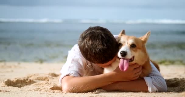 一位中年妇女的画像 一头乌黑的头发和短发躺在海滩上 拥抱和亲吻她的威尔士科吉犬 照顾和爱你的宠物 宠物店横幅 — 图库视频影像