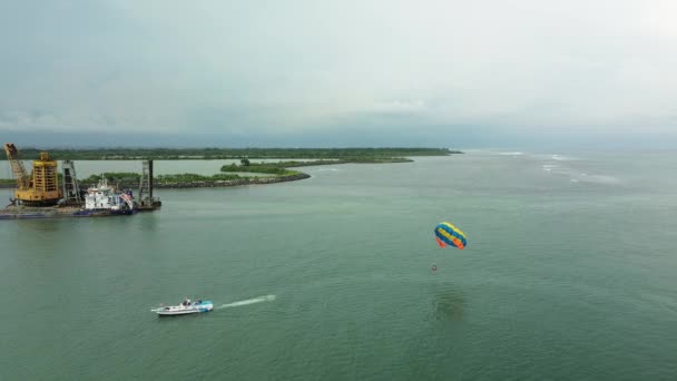 バリのベノア湾で海を渡るパラセーリングの空中ビュー 休暇中のウォータースポーツと水の活動 パラシュートがつながったモーターボート 極端なエンターテイメント — ストック動画