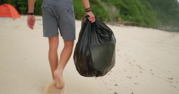 男性のボランティアは プラスチックごみから海岸のビーチをきれいにします 彼はゴミ袋を運んでいる チームワークのクリーニング プラスチック汚染と環境問題のコンセプト — ストック動画