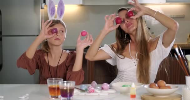 和家人一起庆祝复活节 母亲和女儿戴着兔子耳朵的发夹 坐在桌旁装饰复活节彩蛋 他们用鸡蛋而不是眼睛鬼鬼祟祟地嬉笑着 — 图库视频影像