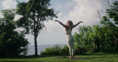 Eşofmanlı genç bir atletik Latin kadın okyanus kıyısındaki bir uçurumda yoga yapıyor. Yoga doğada uygulanır, ruh ve beden sağlığına iyi gelir. Güneş selamı ver asana..