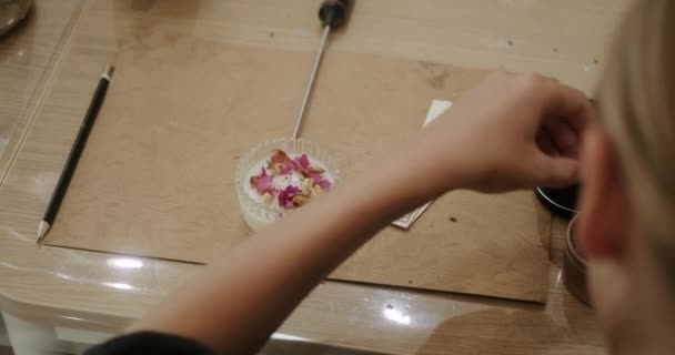 一个少女的特写手拉着一支香味蜡烛在做功课 她在玻璃瓶里创造了一支蜡烛 并用干花装饰它 蜡蜡烛上的花的成分 Diy生产 — 图库视频影像