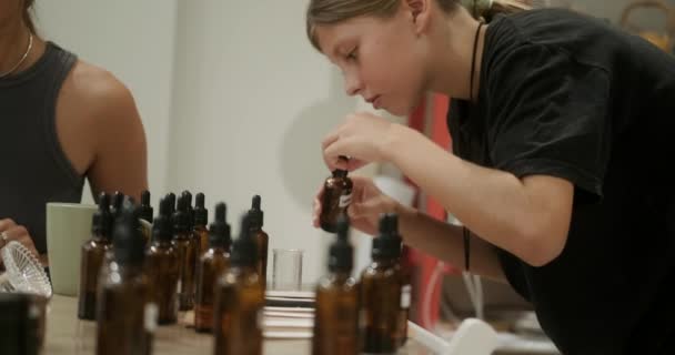 ワークショップで香りのろうそくを作るためのマスタークラスの10代の少女は ろうそくの香りを選択します 彼女は香りの瓶を開け 匂いを嗅ぎ それを別の容器に混ぜました クリエイティブ — ストック動画
