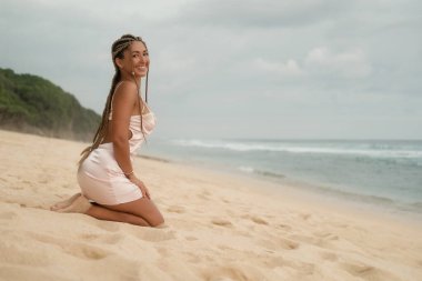 Plajda, ipek pembeli elbisesi olan çekici Latin bir kadın. Okyanusun yanındaki kumda poz veren seksi model. Kadınlığı ve kendine güveni açığa çıkarma kavramı.