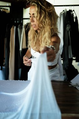 Bir kadın terzi ürünü için kumaş seçer, büyük bir parça beyaz pamuğu sallar ve çalışma masasının üzerine koyar. Bir giyim tasarımcısı kesim için malzeme hazırlar.