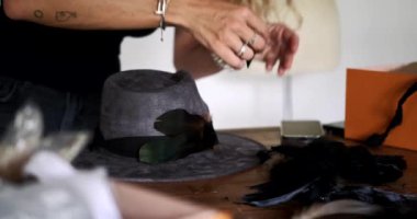 Gri kadife bir şapkayı siyah tüylerle süsleyen ve onları yapıştırıcıyla tuvale bağlayan bir kadın şapkacının elleri. Yeni bir koleksiyon oluşturma süreci bir moda tasarımcısı.