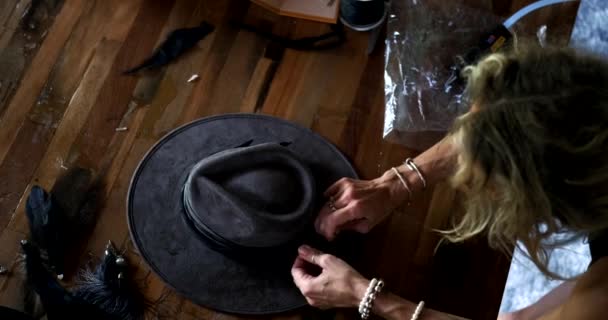 ファブリックの羽 スクラップで灰色の帽子を飾る女性の帽子の木製のテーブルのトップビュー ファッションデザイナーのヘッドドレスとワークスペースを作成するプロセス — ストック動画