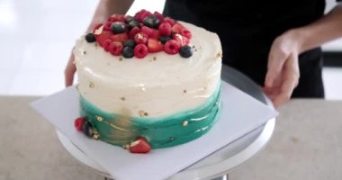 Turkuaz ve beyaz kremayla kaplı, taze böğürtlenlerle süslenmiş bir pastanın üst görüntüsü. Bir pastanenin üretim alanında dönen bir standda duruyor. Güzel doğum günü pastası.