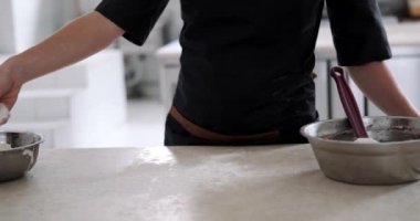 Masanın yüzeyine siyah bir önlüğün arka planına ağır çekimde un serpiştiren bir kadının orta boy resimleri. Bir fırının üretim katında hamur hazırlama işlemi.