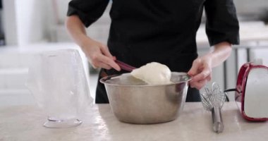 Lokantadaki mutfakta pasta için krema hazırlayan genç bir pasta şefinin ellerine yakın çekim. Demir kaseden tereyağı kremasını spatula kullanarak bir boru torbasına aktarıyor..