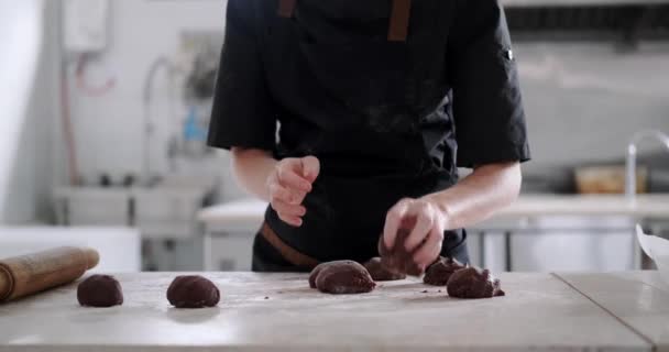 チョコレート生地の小さな部分を形作る若い女性のペストリーシェフの手のミディアムショットは テーブルの上にローリングピンで展開するためにそれらを準備します 菓子で調理するプロセス — ストック動画