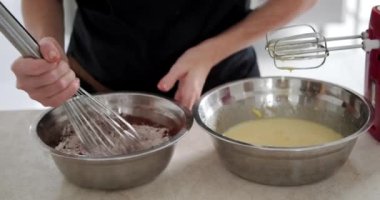 Çikolatalı pasta katmanları hazırlamak için bir kasede un ve kakao tozu yoğuran önlüklü genç bir pasta şefinin yakın çekimi. Hamur hazırlama süreci.