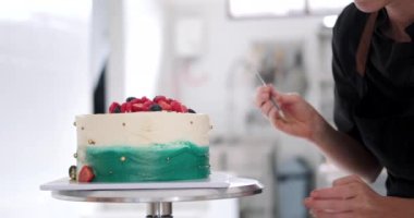 Genç bir kadın pasta şefi taze böğürtlen ve altın parçacıklarıyla bir pasta süslüyor. Bir şekerleme dükkanında profesyonel bir iş. Doğum günü pastası hazırlama süreci.
