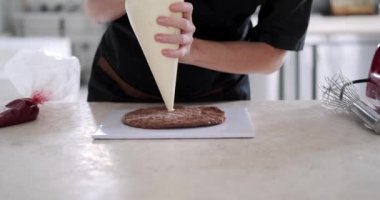 Pasta poşeti kullanarak çikolatalı pastaya tereyağı süren genç bir pasta şefinin ellerine yakın çekim. Profesyonel bir mutfaktaki bir pastanede pasta hazırlama süreci.