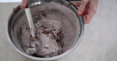 Genç bir kadın pasta şefinin pasta için çikolata hamuru yoğurduğu bir demir kasenin üstünden aşağısına yakın çekim. Şekerlemecideki bir üretim atölyesinde tatlı hazırlama süreci.