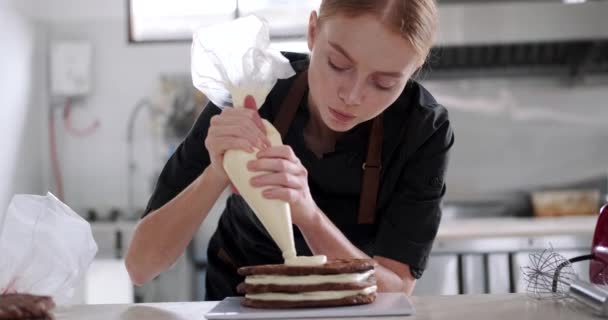 Портрет Молодой Рыжеволосой Кондитерши Наносящей Масляный Крем Слой Шоколадного Торта — стоковое видео