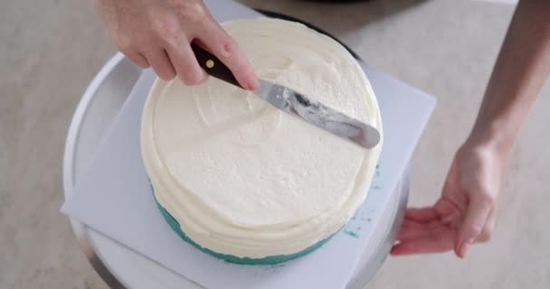 回転スタンドに立っているケーキのトップビュー ペストリーバッグから白いバタークリームを適用する若い女性のペストリーシェフの手のクローズアップ 菓子店での作業のプロセス — ストック動画