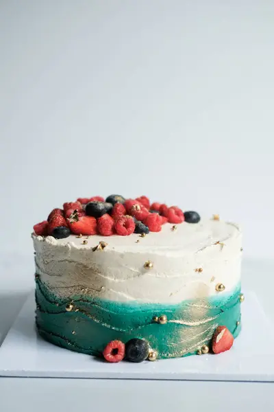 Banner with a cake, which is covered with turquoise and white cream, decorated with fresh berries. It is located on a stand in the production area of the confectionery. Beautiful birthday cake.