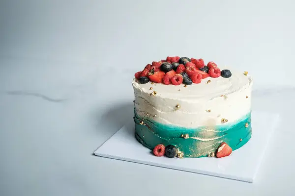 Banner with a cake, which is covered with turquoise and white cream, decorated with fresh berries. It is located on a stand in the production area of the confectionery. Beautiful birthday cake.